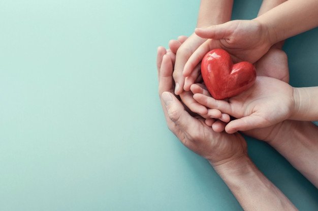 manos adultos y niño sujetando un corazón rojo-salud