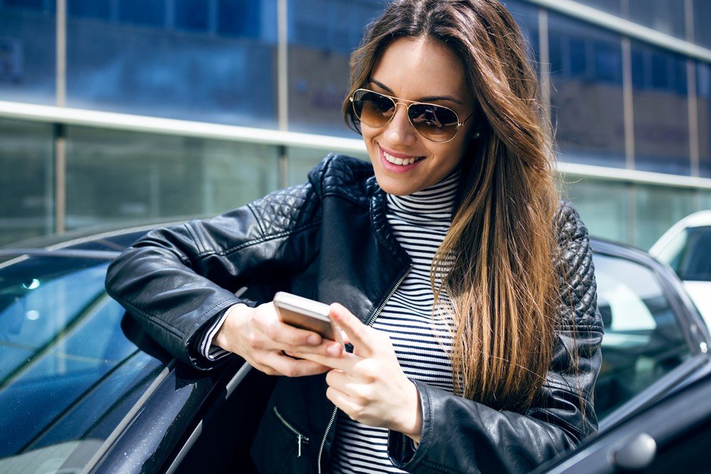 La calidad laboral en Nueva Zelanda - Mujer joven sonriendo mirando el movil - theinfinitynz